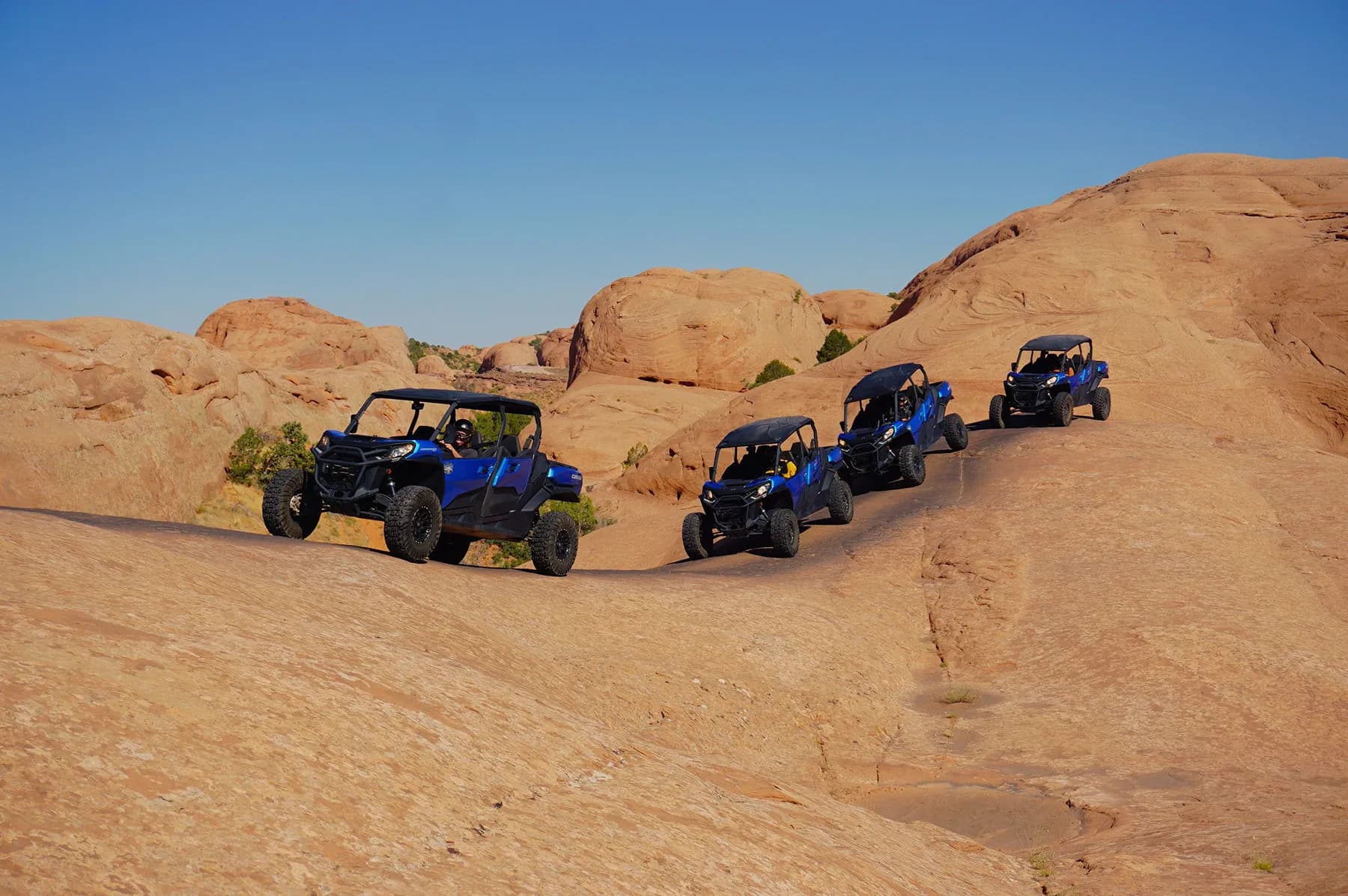 Four blue side-by-sides following each other over rolling slickrock domes
