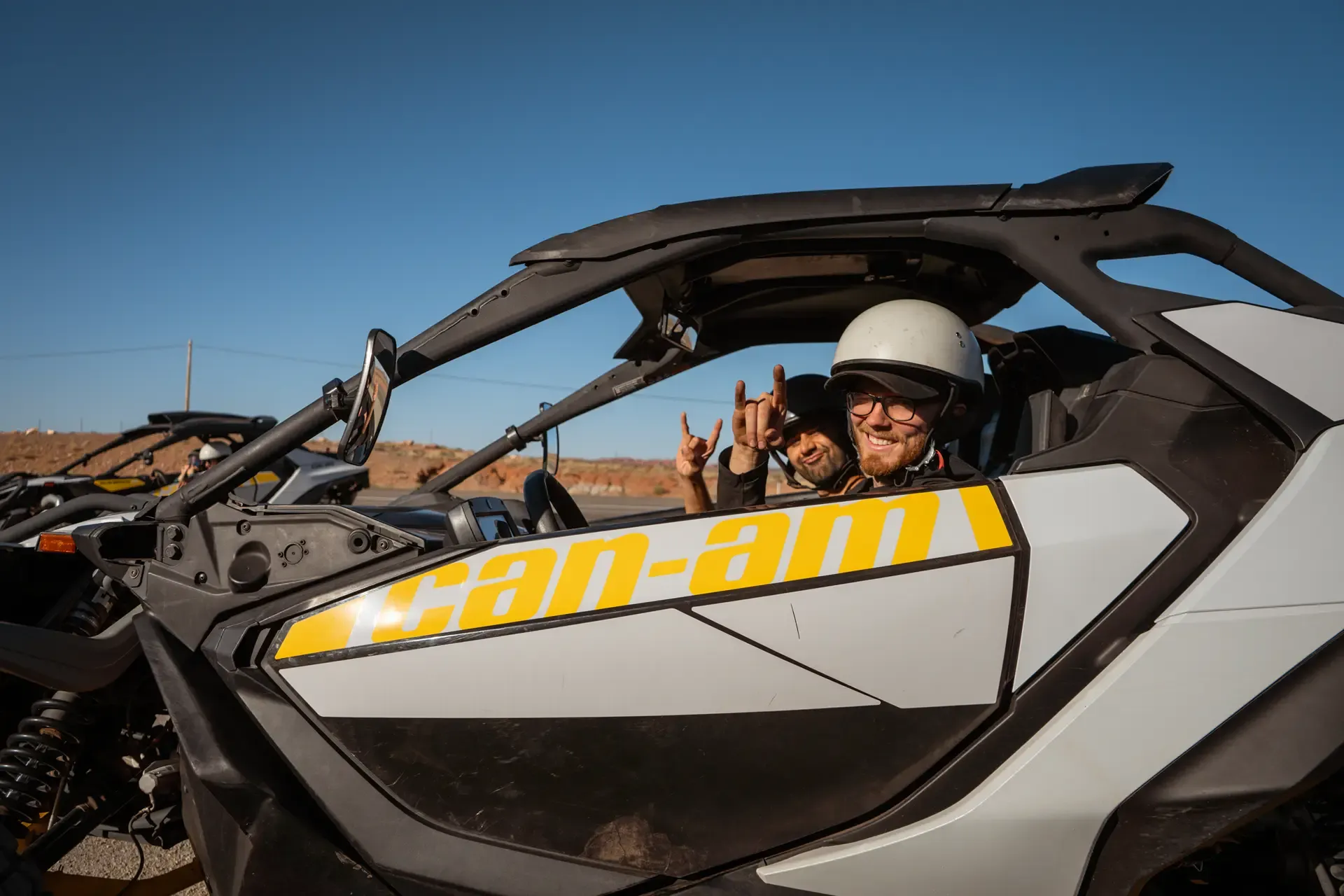 Two guests giving hand signs inside a white Can-Am UTV marked "Can-Am"